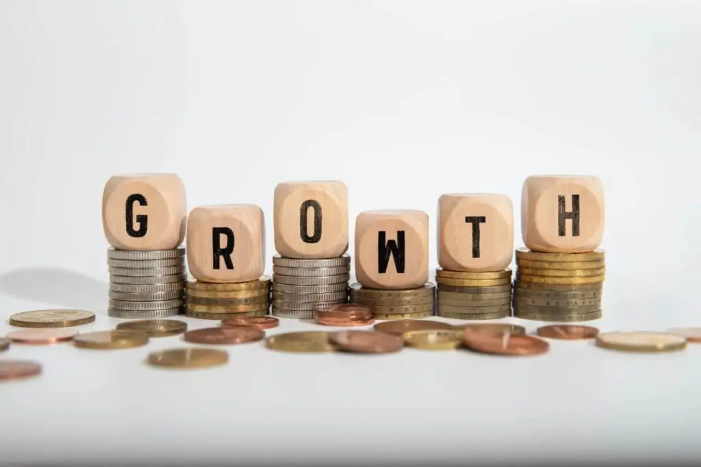Wooden dice spelling "GROWTH" stacked on increasing piles of coins, symbolizing financial growth and career stability.