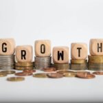 Wooden dice spelling "GROWTH" stacked on increasing piles of coins, symbolizing financial growth and career stability.