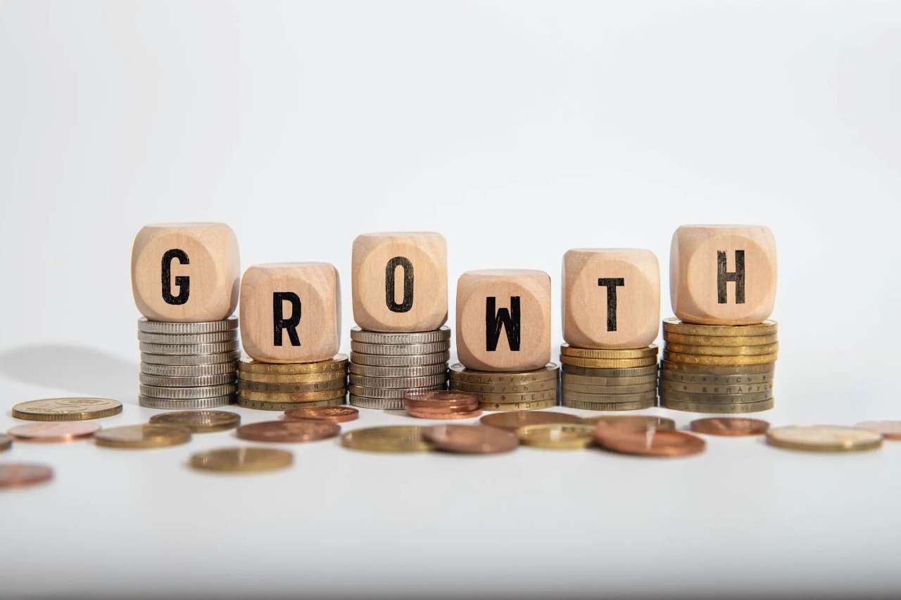 Wooden dice spelling "GROWTH" stacked on increasing piles of coins, symbolizing financial growth and career stability.
